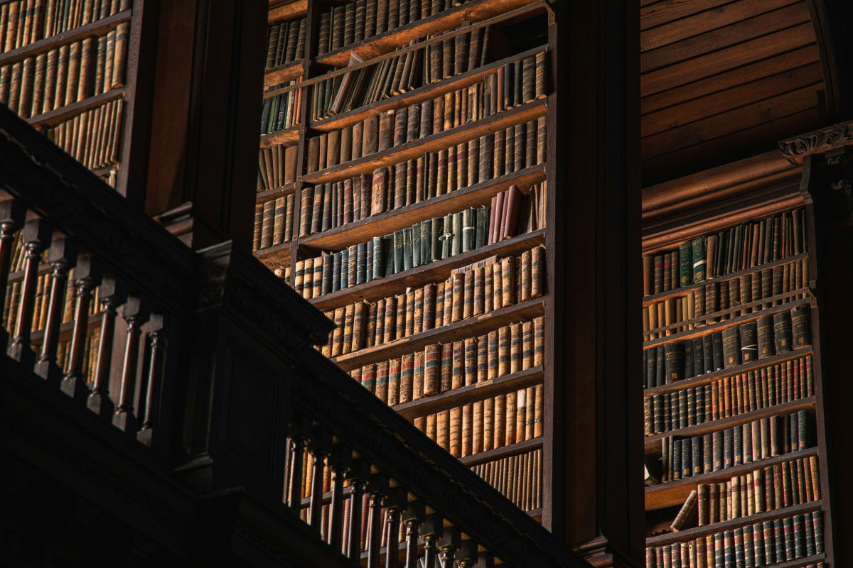 Ein altmodische riesige Bibliothek im Halbdunkel, von der Seite fällt Sonnenlicht auf die Bücher. Foto von Zach Plank